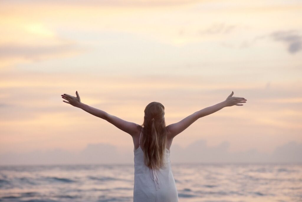 A lady with arms outstretched to a beautiful sunrise sky. Accepting emotions is the key to freedom