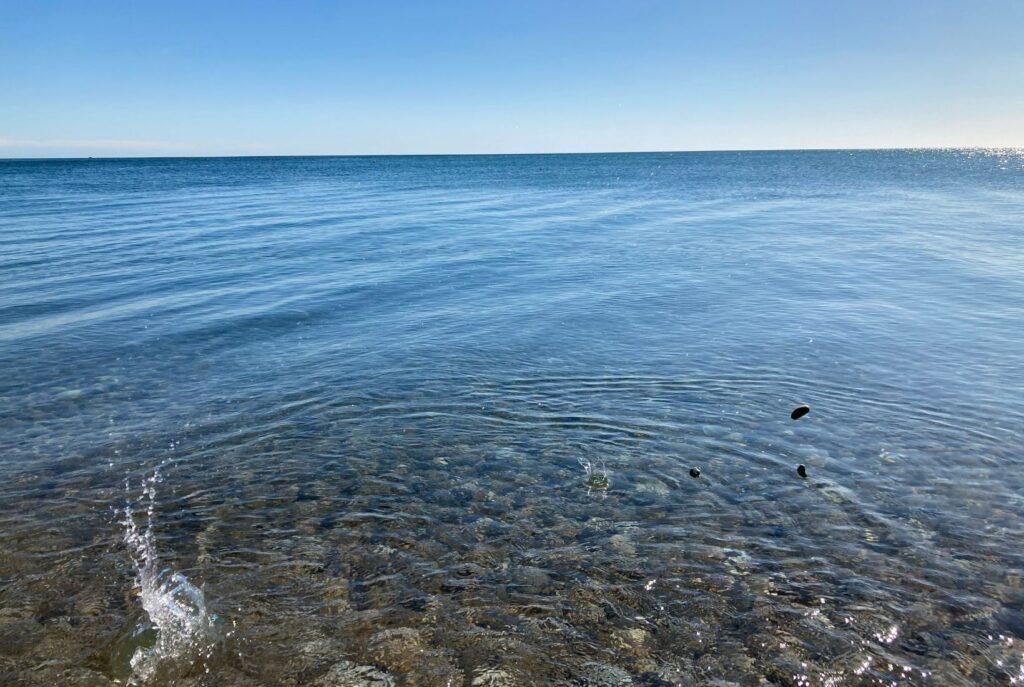 A calm, clear sea with ripples created by throwing pebbles. 